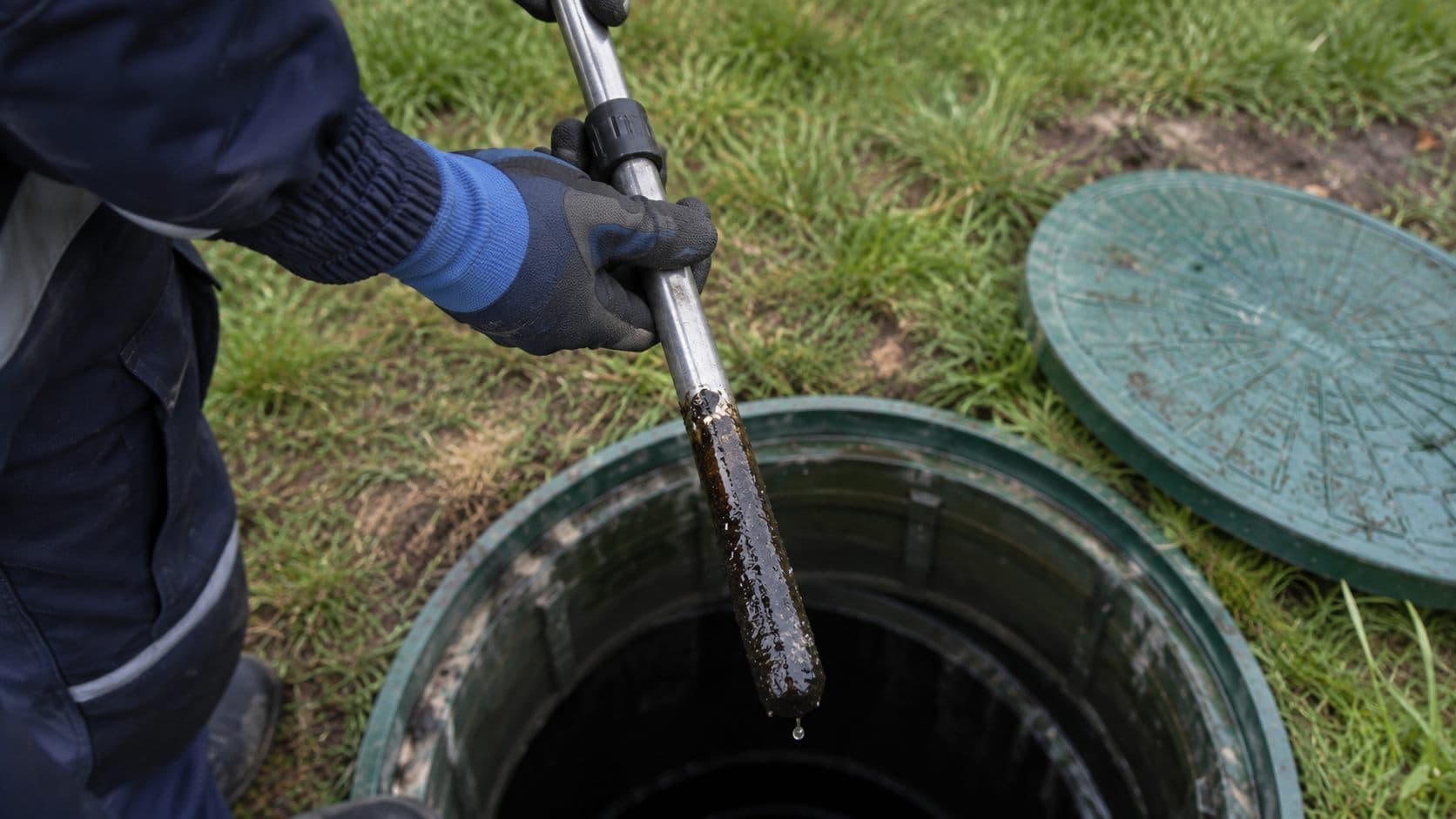 Technik měří tloušťku sedimentu v otevřené šachtě nádrže na dešťovou vodu